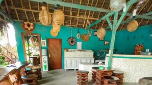 A rustic interior with wooden stools arranged in a semi-circle, a kitchen area with white cabinets, and a ceiling with woven thatch. - Gading Treehouse (Penida Island)