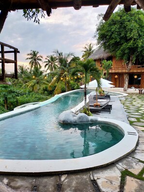 Una piscina con borde de piedra, rodeada de palmeras y una estructura de madera.