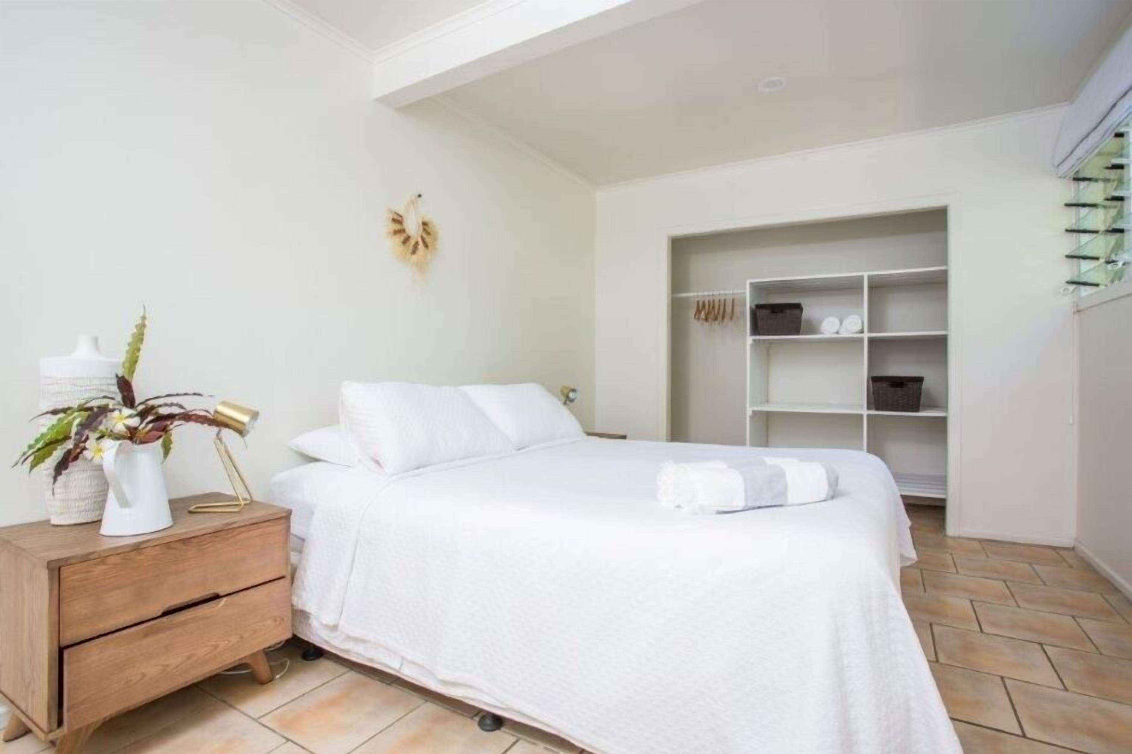 Quarto com cama, mesa de cabeceira, prateleira na parede e um armário.