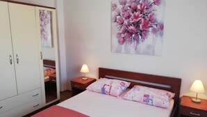 Une chambre à coucher avec un lit, deux tables de chevet avec des lampes, une armoire et un tableau floral accroché au mur.