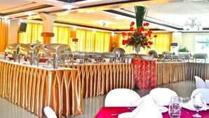 A banquet hall with round tables, a buffet setup, and a floral centerpiece. - Villa Maria Luisa Hotel (Tandag)