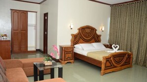 A bedroom with a wooden bed, a wooden wardrobe, a small table, and a sofa. - Villa Maria Luisa Hotel (Tandag)