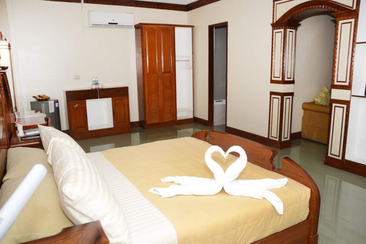 Habitación de hotel con cama, armario de madera y baño a la vista a través de una puerta abierta.