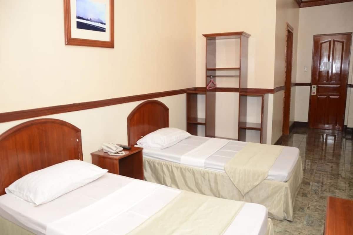 Habitación de hotel con dos camas, un armario de madera, una mesita y un cuadro en la pared.