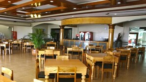 A spacious dining area with wooden tables and chairs, a central bar area, and a potted plant. - Villa Maria Luisa Hotel (Tandag)