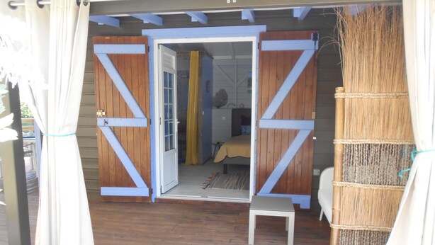 Una habitación con piso de madera, una cama con cubrecama amarillo y una mesita blanca pequeña.