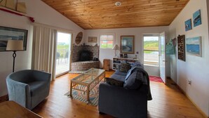 A cozy living room with a fireplace, a ceiling fan, and a view of the outdoors. - Summer Fun on Sandy Beach, Warm Water (Port Hood)