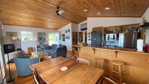 A cozy living room with a wooden ceiling, a fireplace, a sofa, and a dining table with chairs. - Summer Fun on Sandy Beach, Warm Water (Port Hood)