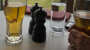 A table with glasses of beer and water, a salt and pepper shaker, and a view of a golf course and ocean through a window. - Summer Fun on Sandy Beach, Warm Water (Port Hood)
