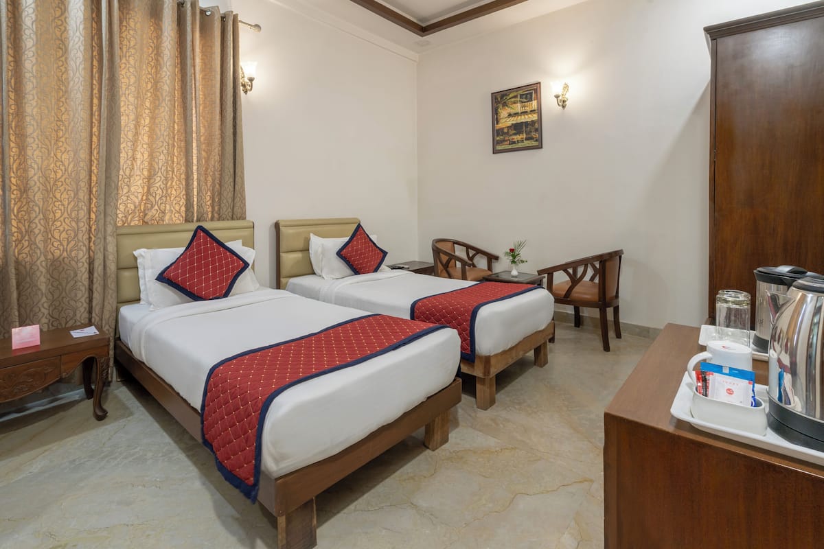 Habitación de hotel con dos camas, un escritorio de madera, una silla, una mesita y una tetera.