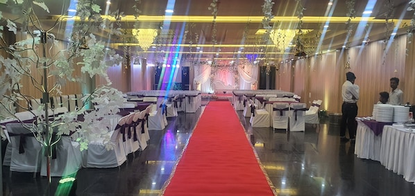 Un salón de banquetes con pasillo de alfombra roja, manteles blancos y candelabros.