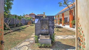 Une cour avec une statue de Bouddha, un sentier en pierre et un bâtiment aux colonnes orange.