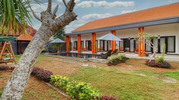 Un hôtel moderne doté d’une piscine, de piliers orange et d’un jardin bien entretenu.