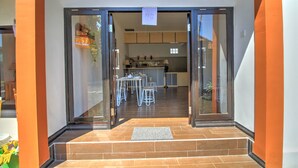 Une cuisine moderne avec un coin repas, comprenant une porte-fenêtre coulissante, un sol carrelé et un petit espace extérieur aménagé pour s’asseoir.