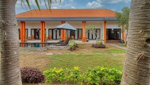 Un bâtiment moderne avec des piliers orange, une piscine et un espace de repos abrité.