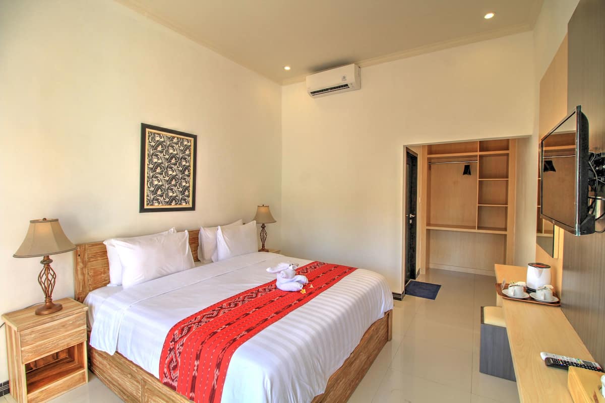 A hotel room with a bed, bedside lamps, a TV, a desk with a remote, and a wardrobe.