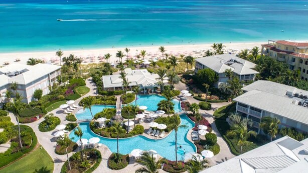 Ett semesterkomplex med en central pool, utsikt över stranden och flera byggnader.