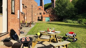 En trädgård med en grill, ett picknickbord och utsikt över en byggnad i tegel med valv.