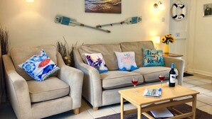 Ett vardagsrum med två beige soffor, ett soffbord i trä och en tavla som föreställer en solnedgång över havet.