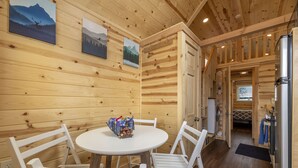 L’intérieur d’un chalet en bois, avec une table ronde, des chaises blanches et un panier rempli d’objets posé sur la table.