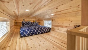 Une chambre dans une cabane en bois, avec un lit, des murs en bois et un plafond en pente.