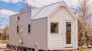 Une petite maison mobile de plain-pied, dotée d’un toit à deux versants et d’une porte d’entrée avec une fenêtre.