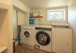 Een kleine wasruimte met twee wasmachines, een droogrek en een raam dat zorgt voor natuurlijk licht.
