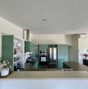 A modern kitchen with teal cabinetry, stainless steel appliances, and a central island.