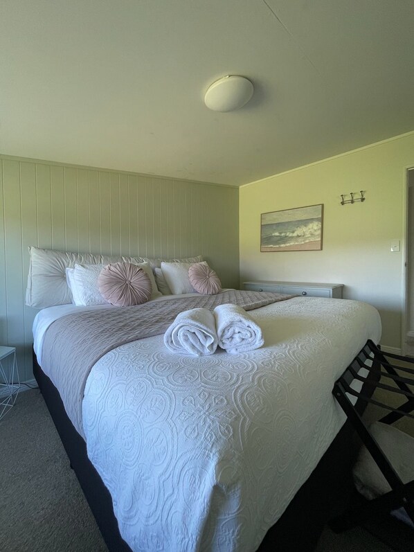 A neatly made bed with rolled towels, a bedside table, a wall-mounted light, and a painting. - Natural Lake and widespread views with family sized apartment/house (Motueka)
