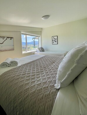 A bedroom with a large bed, a window with a view, and a wall-mounted artwork.