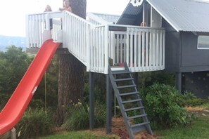 Een houten speelconstructie met een rode glijbaan en een ladder.