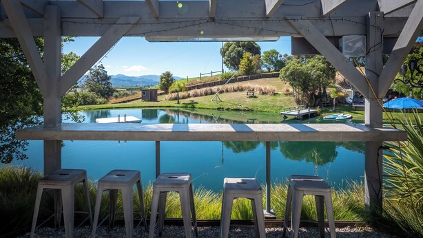 A wooden pergola with a view of a calm pond and a grassy area with hay bales.