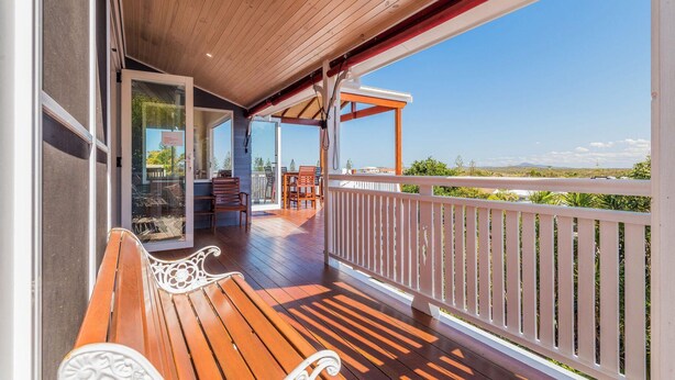 Una terraza de madera con barandilla blanca, un banco y una mesa con sillas.