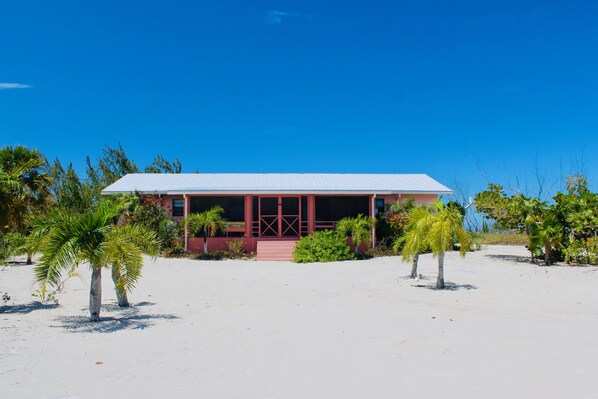 A building with a red facade and a white roof, surrounded by palm trees and sand.