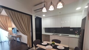 A modern kitchen with white cabinets, a black countertop, and a sink. There is a dining table with plates and a flower vase. - Almas Puteri Harbour By Squarenest (Iskandar Puteri)