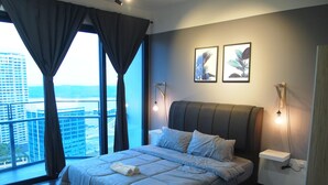 A modern bedroom with a large bed, a view of the city, and two wall-mounted light fixtures. - Almas Puteri Harbour By Squarenest (Iskandar Puteri)