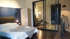 A modern bedroom with a large bed, a wardrobe, a desk with a television, and a sliding glass door leading to a living area. - Almas Puteri Harbour By Squarenest (Iskandar Puteri)