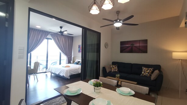 A modern hotel room with a dining area, a sofa, and a ceiling fan. - Almas Puteri Harbour By Squarenest (Iskandar Puteri)