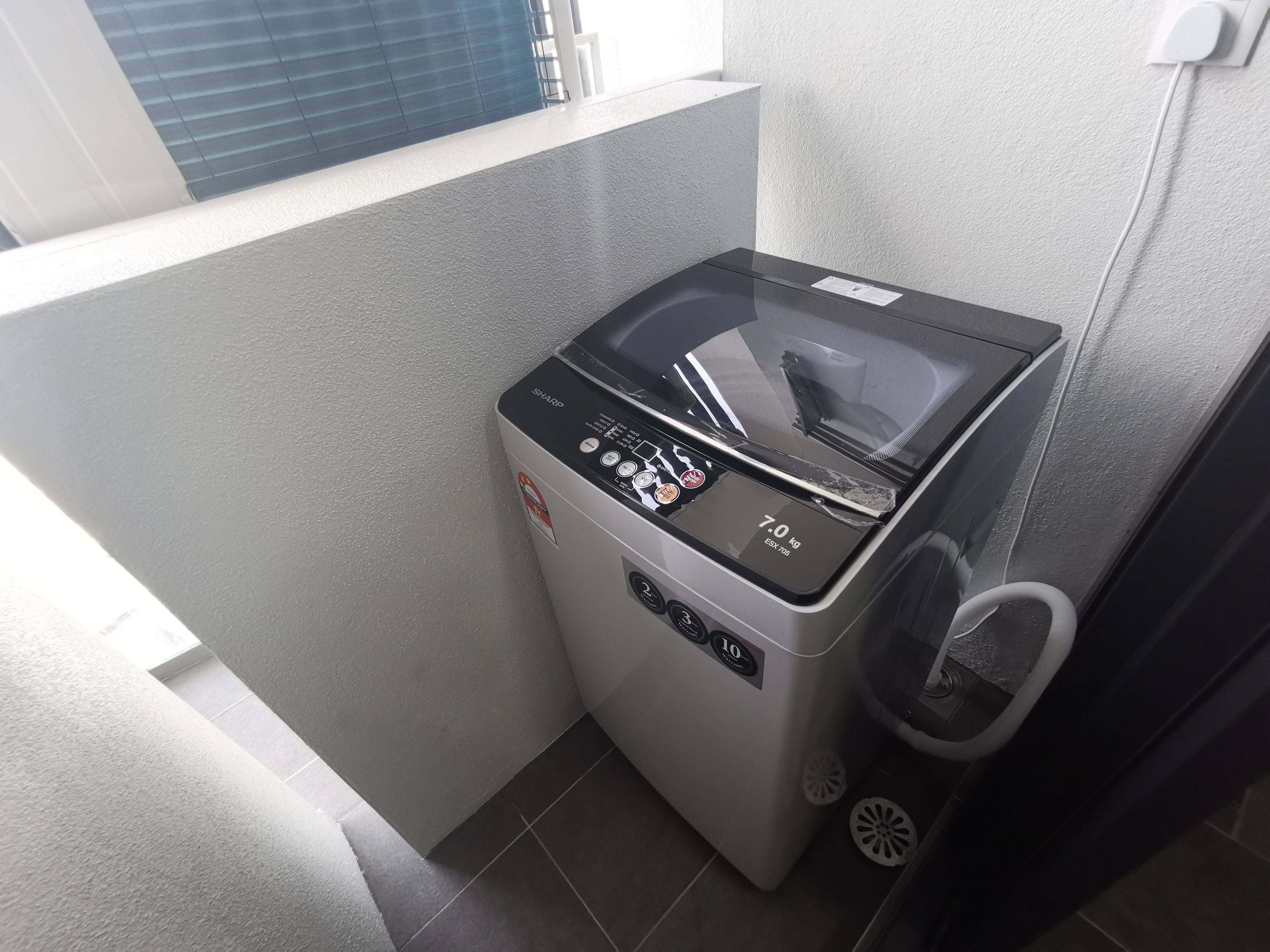 A compact, modern washing machine in a small laundry area with a window and a power outlet.
