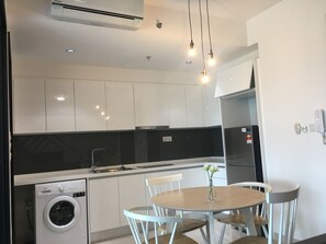 Una cocina moderna con armarios blancos, lavadora incorporada y una mesa de comedor redonda con sillas.