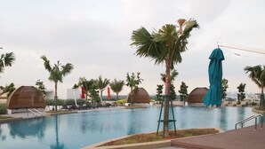 A swimming pool with lounge chairs and palm trees. - Almas Puteri Harbour By Squarenest (Iskandar Puteri)