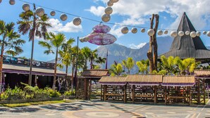 An outdoor area with a patterned pavement, palm trees, and a building with a traditional roof. - Hiker's Camp at Toya Devasya (Kintamani)