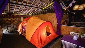 A room with a large tent-like structure, a brick wall, and a table with a purple tablecloth. - Hiker's Camp at Toya Devasya (Kintamani)