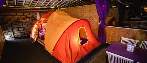 Una habitación con una gran estructura similar a una tienda de campaña, una pared de ladrillo y una mesa con mantel morado.