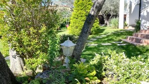 Ein Garten mit einem weißen Laternenpfahl, verschiedenen Sträuchern und einer Rasenfläche.
