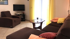 Ein Wohnzimmer mit einer Couch, einem Sessel, einem Fernseher und einem Tisch mit einer Vase.