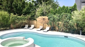 A swimming pool with a hot tub, surrounded by lounge chairs and a wooden fence.