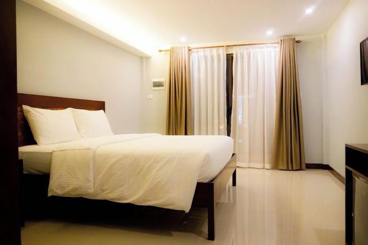 Une chambre d’hôtel avec un lit, des rideaux, un téléviseur à écran plat et un plancher de couleur claire.