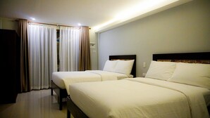 Ein Hotelzimmer mit zwei Einzelbetten, einem großen Fenster mit Vorhängen und einem Flachbildfernseher.