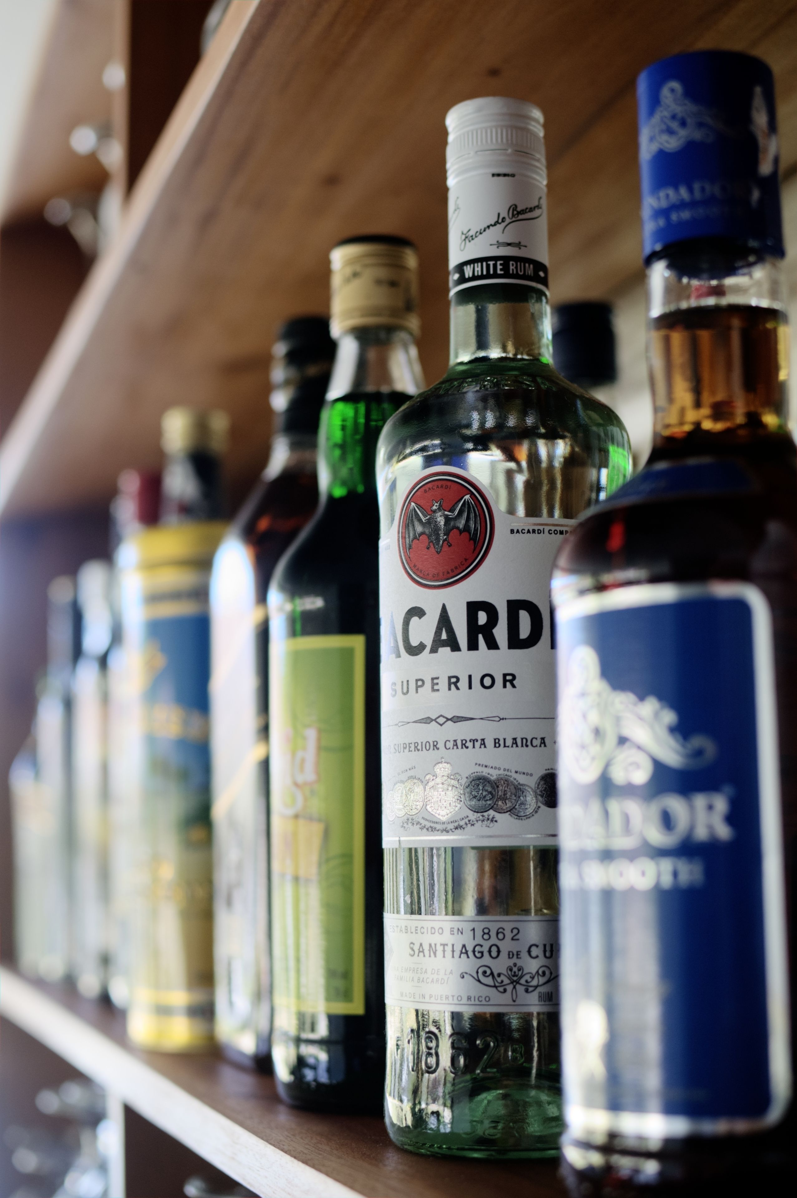 En hylla med olika sorters alkoholdrycker, inklusive en framträdande flaska med etiketten ”Cardo Superior”.